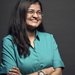Mansi Kasliwal smiles with her arms crossed. She wears a button-down shirt in front of a black backdrop.