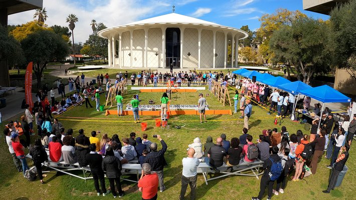 A crowd of people watch the ME72 competition in front of the Beckman Auditorium, a round white building with columns