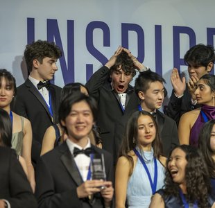 Regeneron Science Talent Award finalists stand on risers as Matteo Paz, back row, looks shocked at his first-place win.