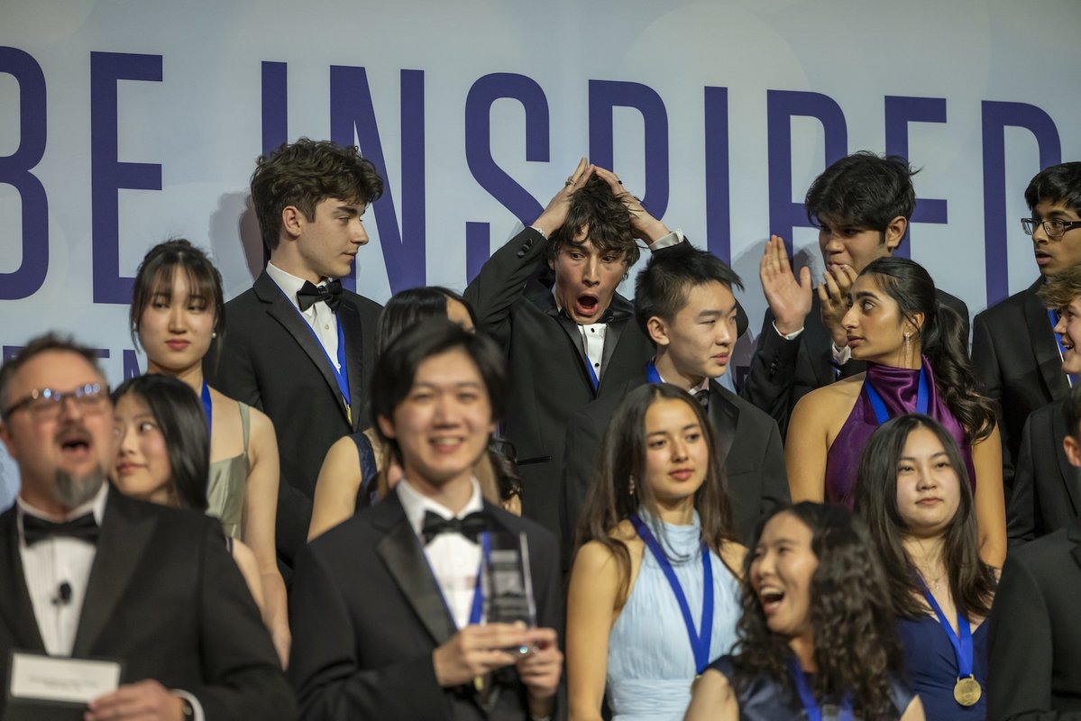 Regeneron Science Talent Award finalists stand on risers as Matteo Paz, back row, looks shocked at his first-place win.