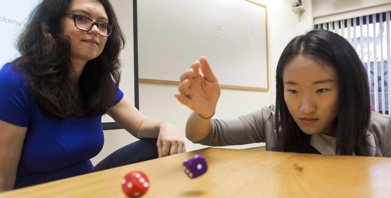 Marina Agranov sits at a table while a student tosses dice.