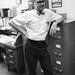 Professor Arden Albee, in 1967, stands by a file cabinet wearing a white short-sleeved shirt and a bowtie.