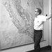 Arden Albee stands, in a white short-sleeved shirt and bow tie, looking at a very large relief map of the state of California.