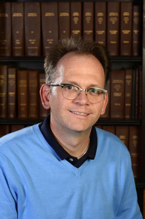 Brian Stoltz in front of a bookshelf.