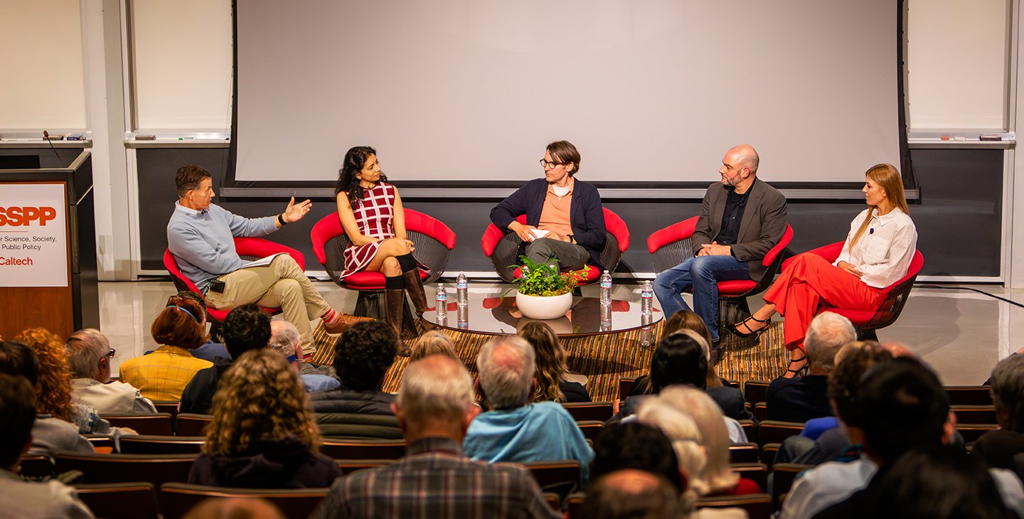 Panel of 5 people in chairs in front of an audience