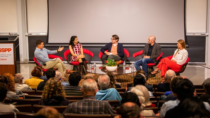 Panel of 5 people in chairs in front of an audience