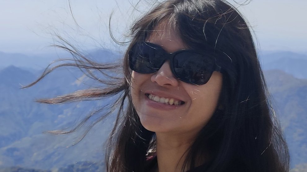 With clouds and mountains in the background, a person smiles at the camera