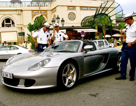 Two men sit in a Porsche while a police officer talks to them. A few more officers stand nearby, looking on.