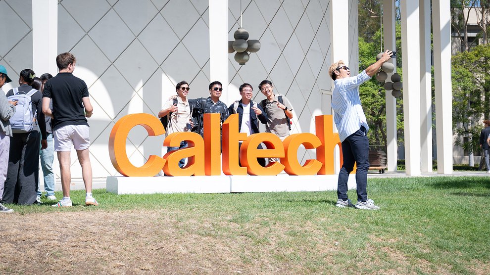 A group of students poses for a photo with large orange block letters that spell out "Caltech."