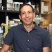 A portrait of Michael Elowitz. He wears a short-sleeve button-down shirt and is in his lab.