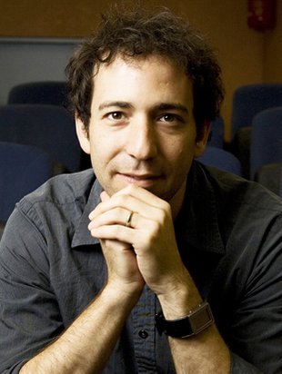 A portrait of Michael Elowitz. His hands are folded in front of his face and he wears a button-down shirt.
