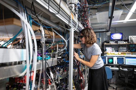 Hannah works in a lab filled with optical devices and chords.