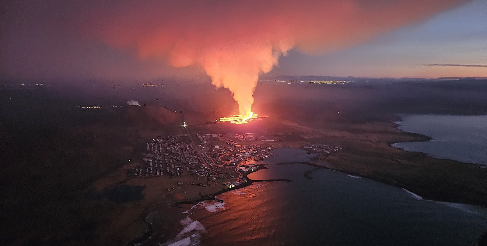 A red plume of lava near a town on a coastline
