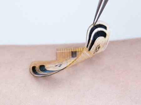 A thin U-shaped sensor device being lifted up with tweezers to show how thin it is.