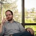 Professor of Political Science Michael Gibilisco sits in a chair in front of windows showing trees behind him