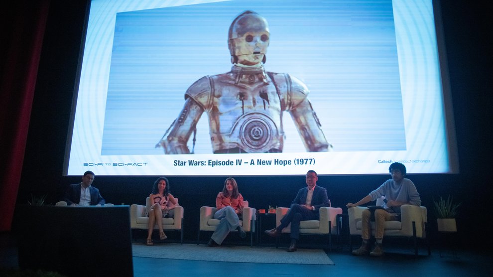 Panelists sit in front of a large screen showing C-3PO from Star Wars.