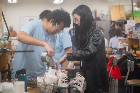 Two students work to repair a white robot with duct tape during the ME72 competition.