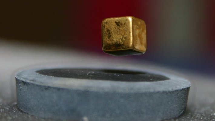 A small magnet levitates above a piece of high-temperature superconductor. The magnet is cube shaped. The superconductor is covered in frost and surrounded by wisps of vapor.