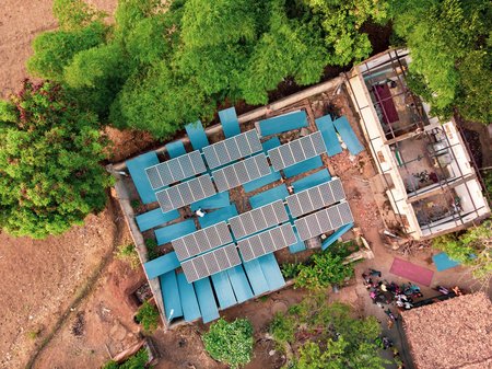 An aerial view of a solar microgrid mostly surrounded by trees and dirt.