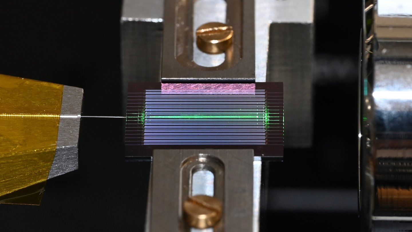 a chip with multiple horizontal channels has one lit up green. An optical fiber extends from the chip to the left.