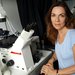 A woman sits by a microscope in a laboratory