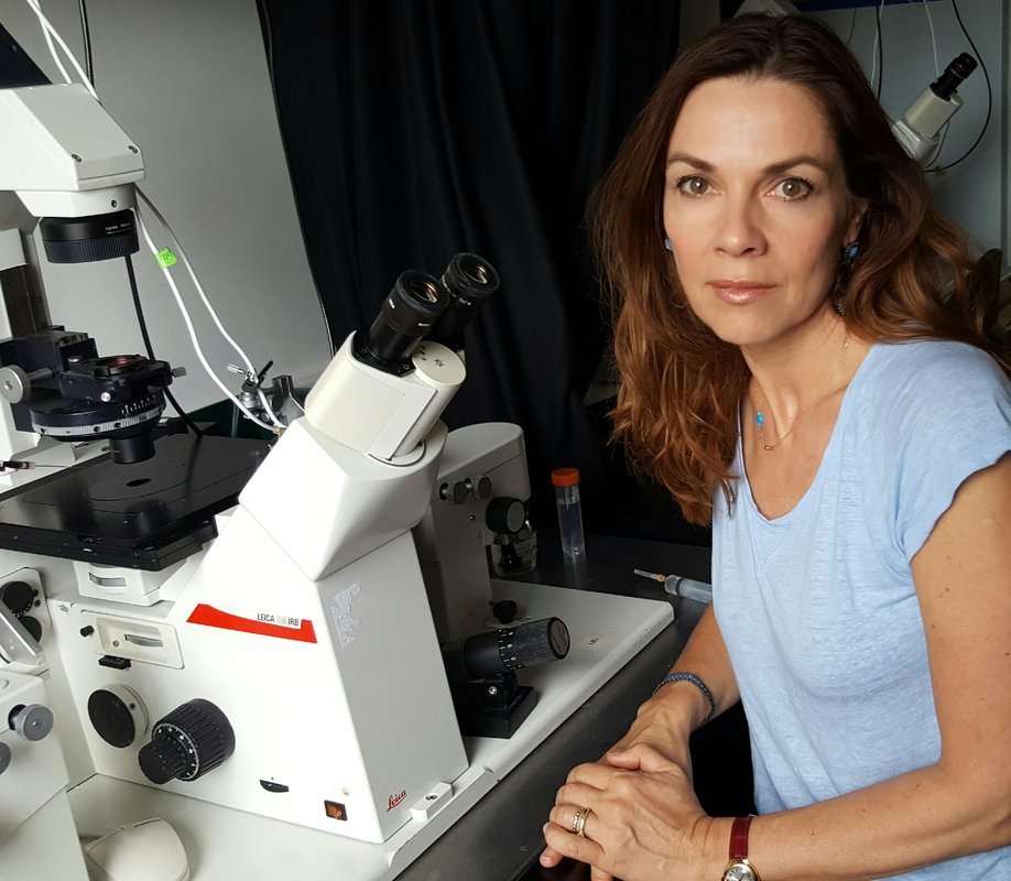A woman sits by a microscope in a laboratory