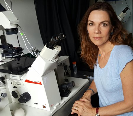 A woman sits by a microscope in a laboratory