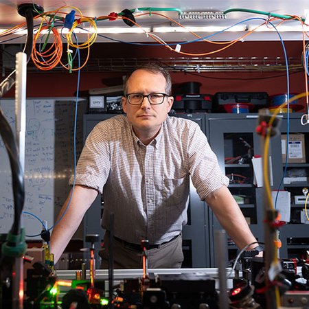 Nick Hutzler of Caltech standing behind machinery and wires