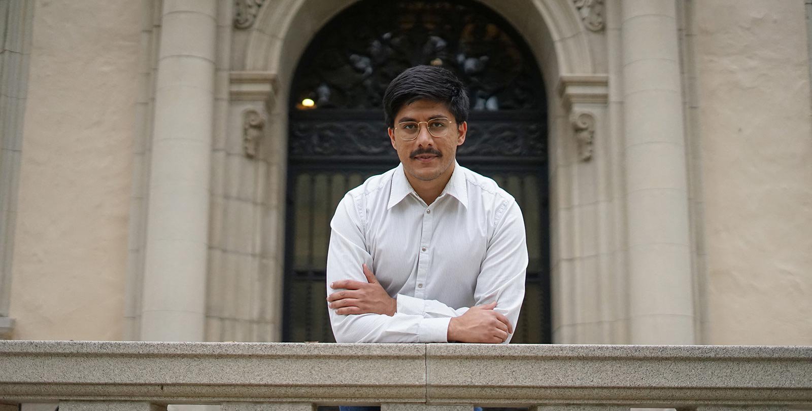 A man with dark hair, glasses, mustache, and white shirt.