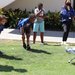 Children with one adult look at a doglike robot walking on grass.