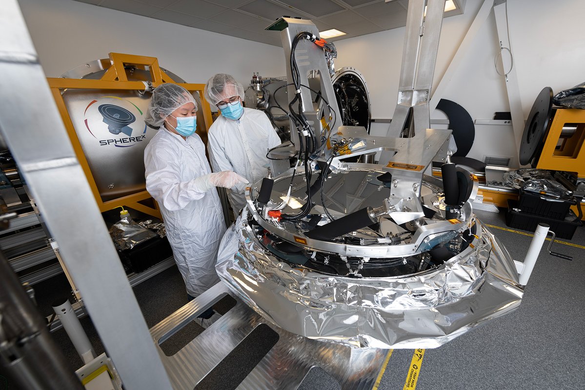 Engineers in cleanroom suits work on the instrument.