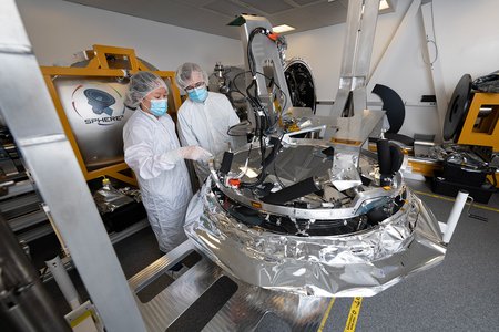Engineers in cleanroom suits work on the instrument.