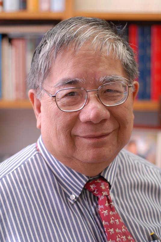Sunney Chan smiles at the camera without showing his teeth. He wears glasses, a blue and white striped shirt, and a red tie with horses jumping over a gate.