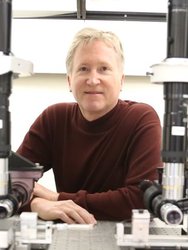 A portrait of Kerry Vahala surrounded by optical devices.