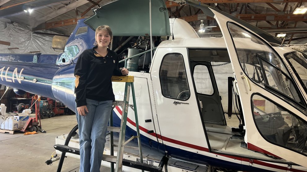 A person stands on a ladder in front of a helicopter.