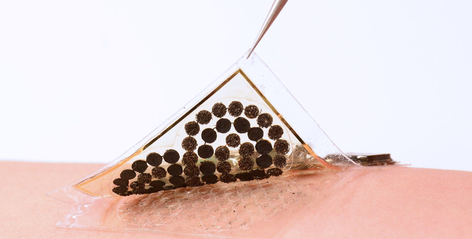 A pair of tweezers peels a sample of a electronic skin from the skin of an arm.