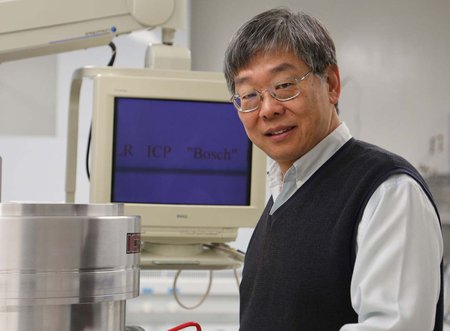 Yu-Chong "Y.C." Tai stands in a laboratory smiling at the camera. A computer monitor is in the background.