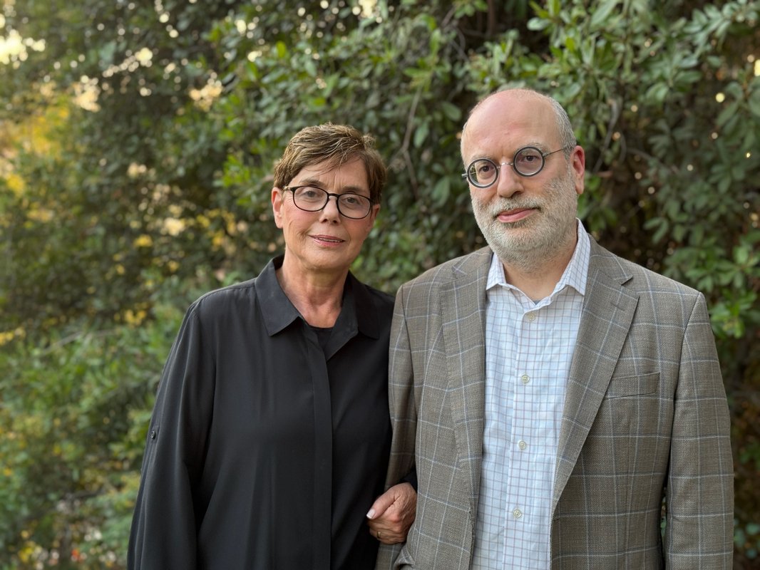 Diana Kormos-Buchwald and Michael R. Gordin stand next to one another arm-in-arm. Kormos-Buchwald wears a long black shirt and Gordin wears a tan plaid sportsjacket.