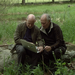 two men sit in a field looking at a computer together