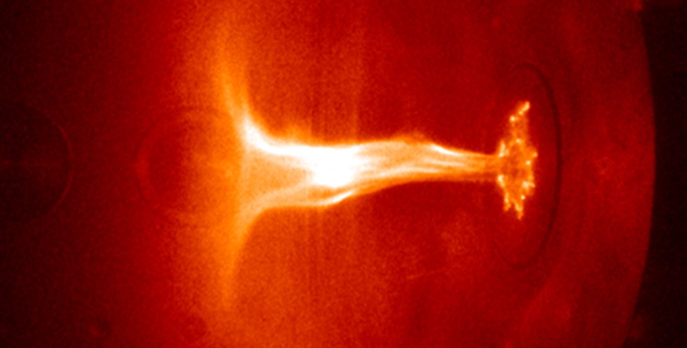 A flame-like jet of plasma takes on a shape reminiscent of an umbrella or mushroom inside a vacuum chamber.