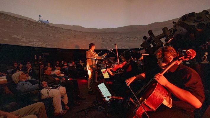 An orchestra plays the Mars Symphony while audience members look up at images from the Red Planet.