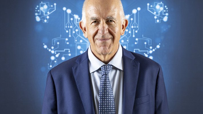 a man in a suit smiles with computer schematics in the background in the shape of a butterfly
