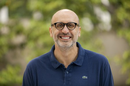 A portrait of Antonio Rangel. He wears glasses and a blue polo. Green trees are in the background