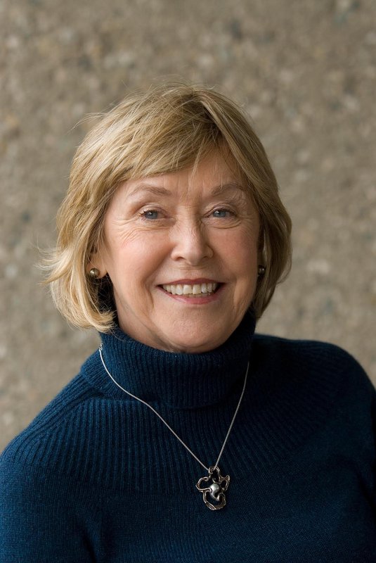 A woman with blonde hair and a blue turtleneck smiles for a portrait