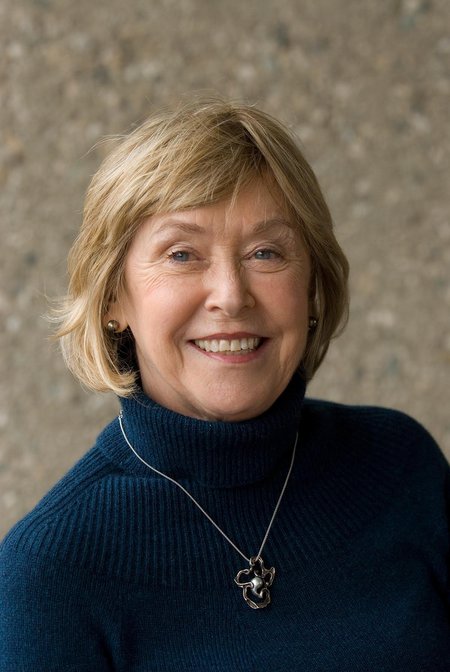 A woman with blonde hair and a blue turtleneck smiles for a portrait