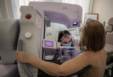 Photo of a patient getting a mammogram with a medical professional in a blue surgical mask facilitating
