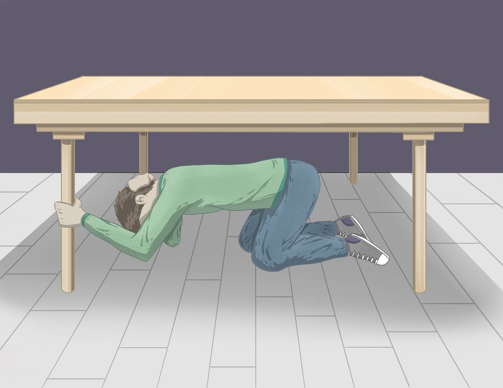 A person sheltering under a table, depicted practicing drop, cover, and hold on during an earthquake.