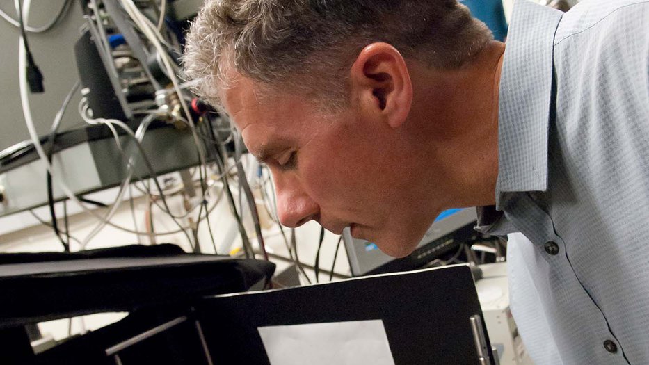 Man bending over scientific equipment using tweezers to adjust
