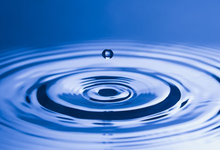 Photo of a single drop of water splashing and a ripple forming around it