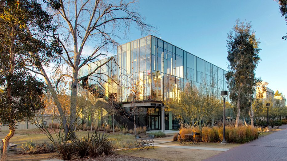 Glass building with trees, shrubs, and empty tables and chairs in the foreground
